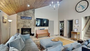 A living room with a stone wall, a fireplace, a large TV, and a chandelier.