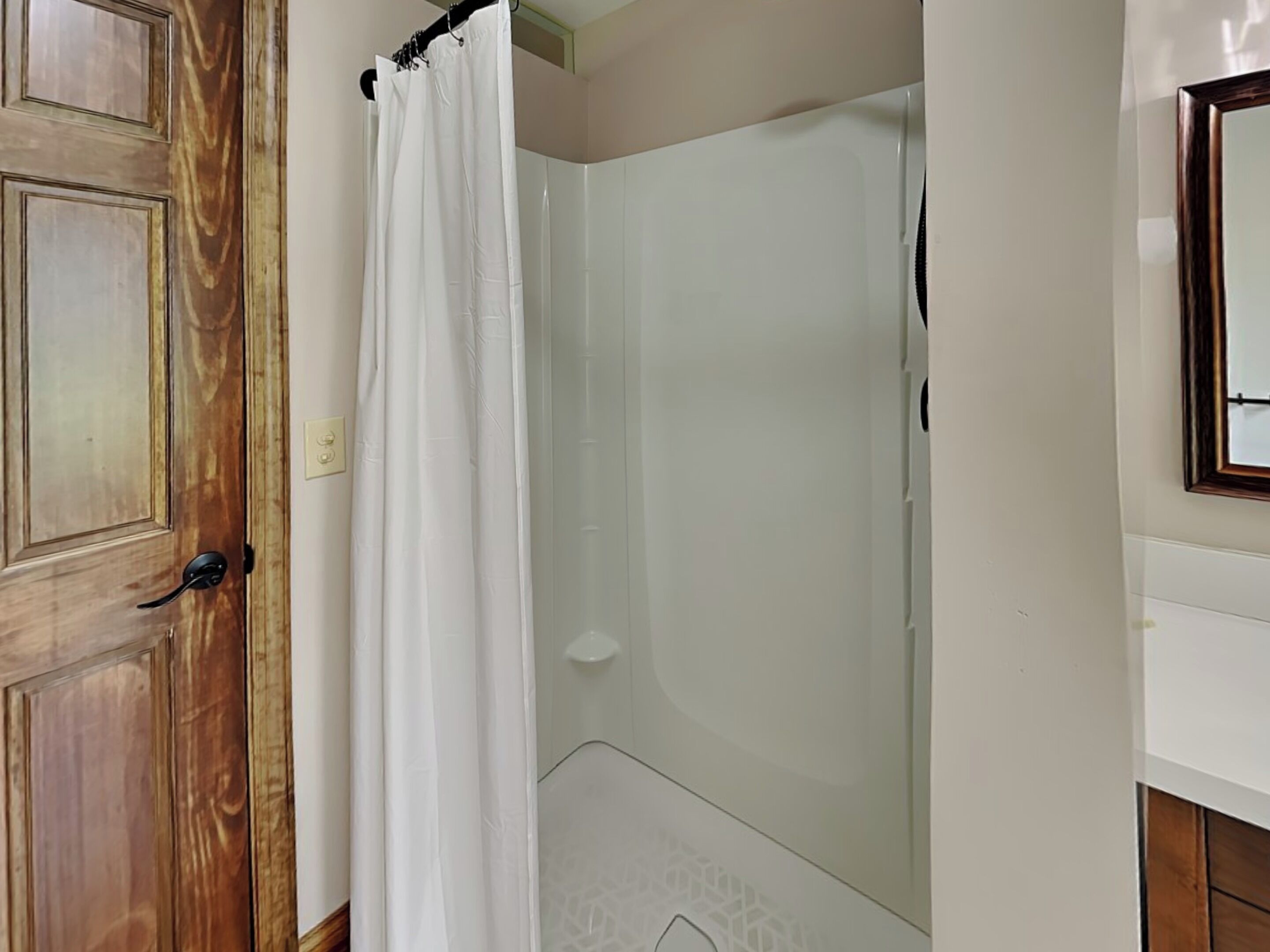 A bathroom with a wooden door, a white shower curtain, and a glass shower enclosure.