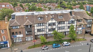 A multi-story building with a mix of residential and commercial spaces, featuring a prominent clock tower and a visible storefront on the ground floor. - City Service Lets - Large Cheam 1 bed with parking - Long stays welcome (London)