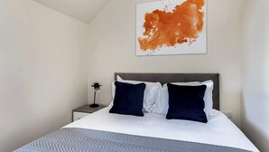 A modern hotel room with a neatly made bed, a bedside table with a lamp, and a large abstract painting on the wall. - City Service Lets - Large Cheam 1 bed with parking - Long stays welcome (London)