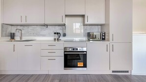 A modern kitchen with white cabinets, a built-in oven, a microwave, and a sink. - City Service Lets - Large Cheam 1 bed with parking - Long stays welcome (London)