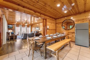 Un intérieur en bois comprenant une table à manger pour quatre personnes, un banc et un réfrigérateur.