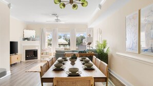A dining area with a long table set for six, a fireplace, a television, and a view of the outdoors.