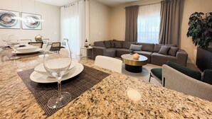 Un salon moderne avec un coin repas, comprenant un comptoir en granit, un canapé, une table basse et une table à manger, le tout agrémenté d’assiettes et de verres.