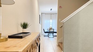 Un couloir avec un comptoir en bois, une plante en pot, une table avec des chaises et un escalier.