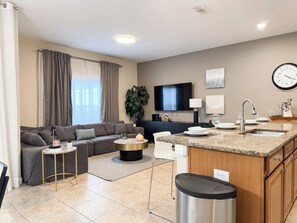 A modern living room with a sofa, coffee table, and TV. There's a kitchen area with a sink, countertop, and cabinets. - Spacious 4-bedroom townhome in brilliant Kissimmee with Private Pool (Kissimmee)