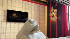Une chambre d’hôtel avec un lit, un téléviseur fixé au mur et une fresque représentant Mickey Mouse.