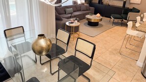 Un salon moderne avec une table à manger en verre, des chaises noires, un canapé, une table basse et un téléviseur.