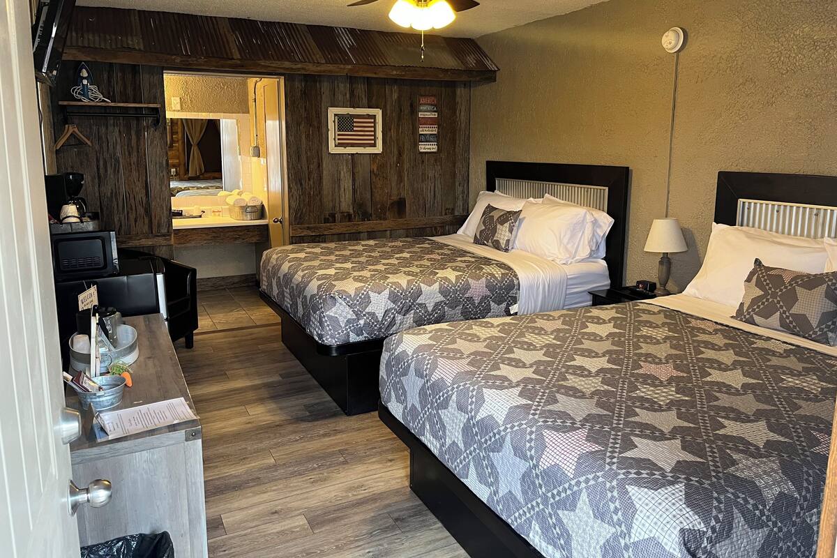 A hotel room with two beds, a desk, a coffee machine, and a ceiling fan.