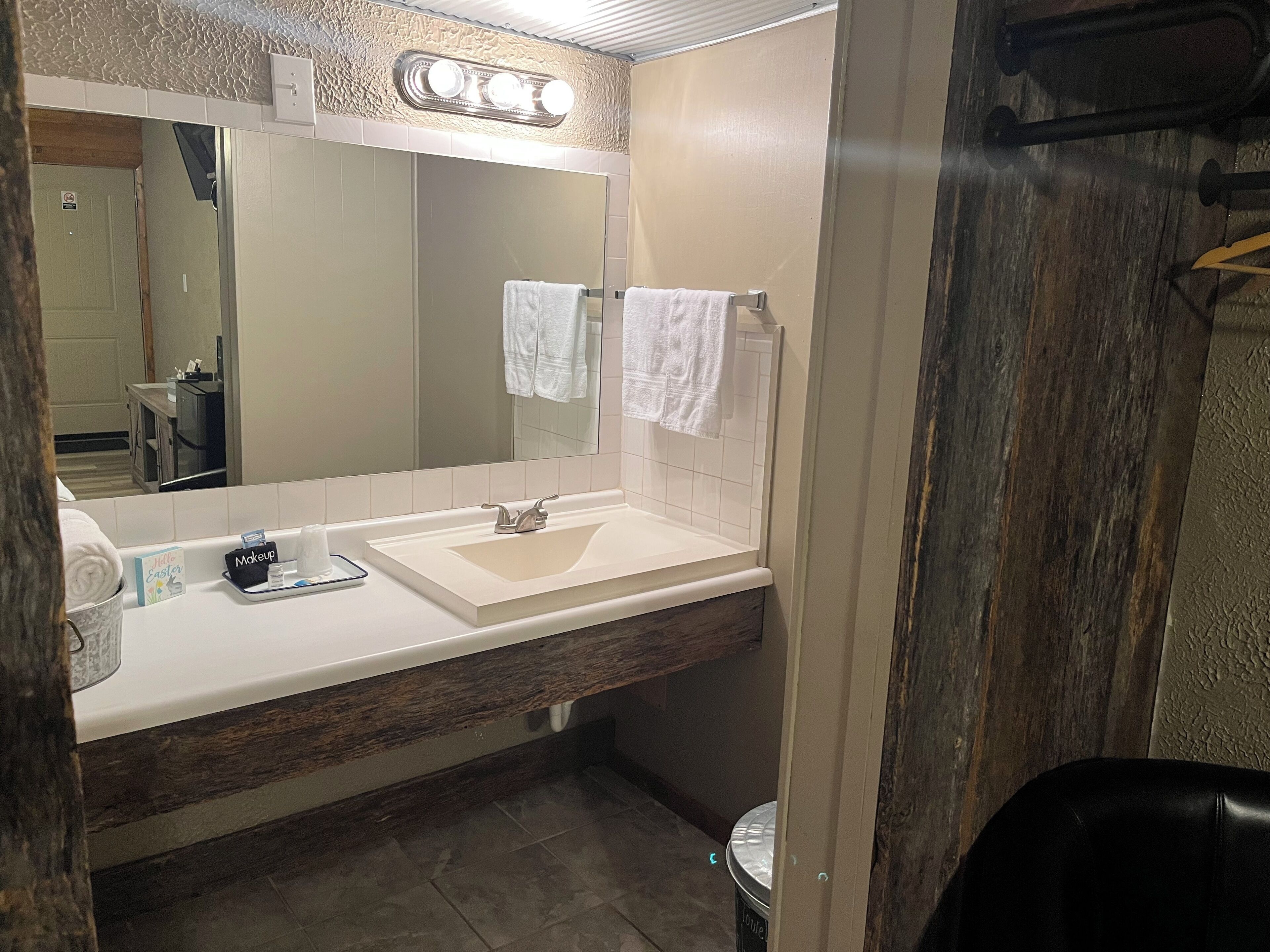 A bathroom with a white sink, a large mirror, and a vanity with a makeup tray.
