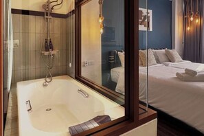 A modern bathroom with a large bathtub, a glass shower enclosure, and a bed with neatly made white linens.