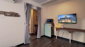 A hotel room with a wooden floor, a small refrigerator, a flat-screen TV mounted on the wall, and a wooden bench. - Belivin'98 Sense of Pier Sathon Residence (Bangkok)
