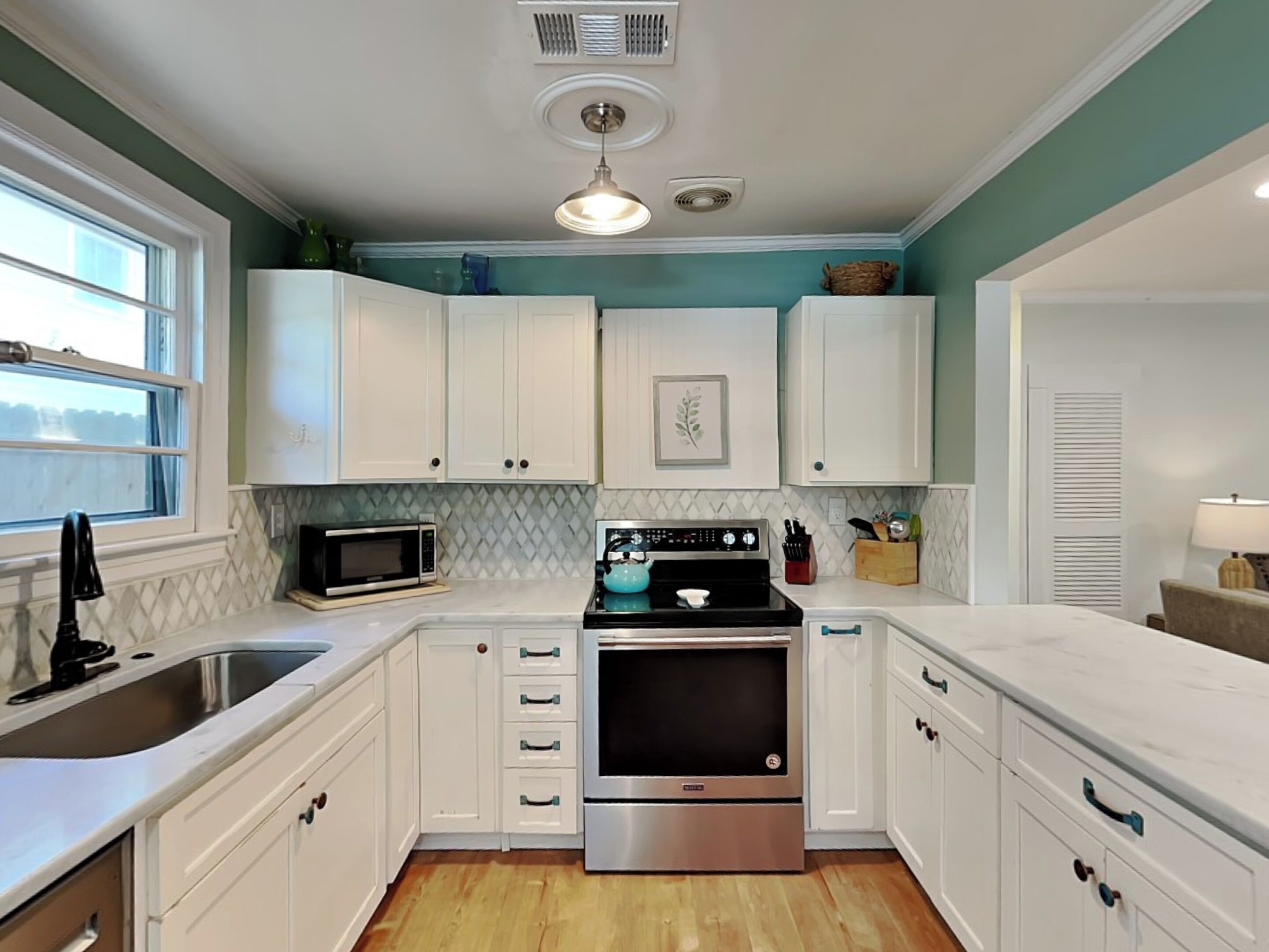 A kitchen with white cabinets, a microwave, a stove, and a sink.
