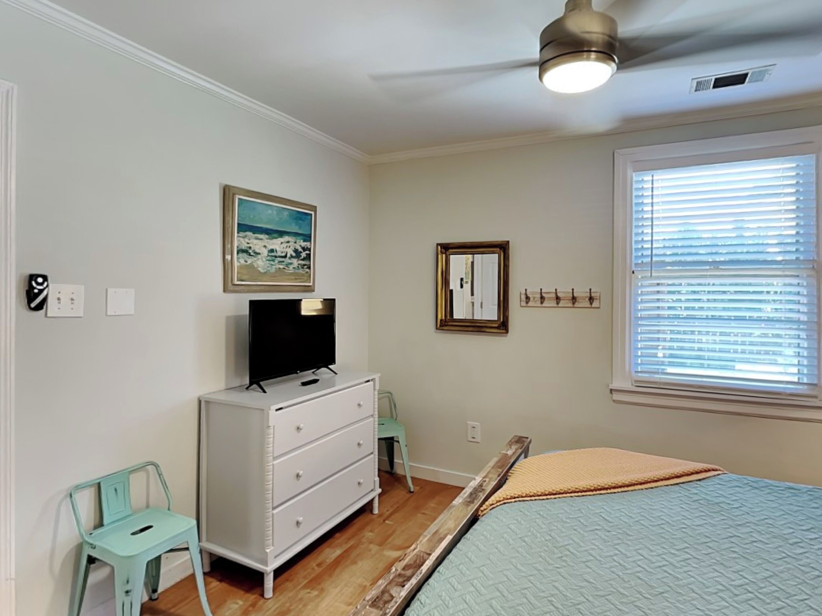 A bedroom with a bed, a dresser, a chair, a ceiling fan, a window with blinds, and a painting on the wall.