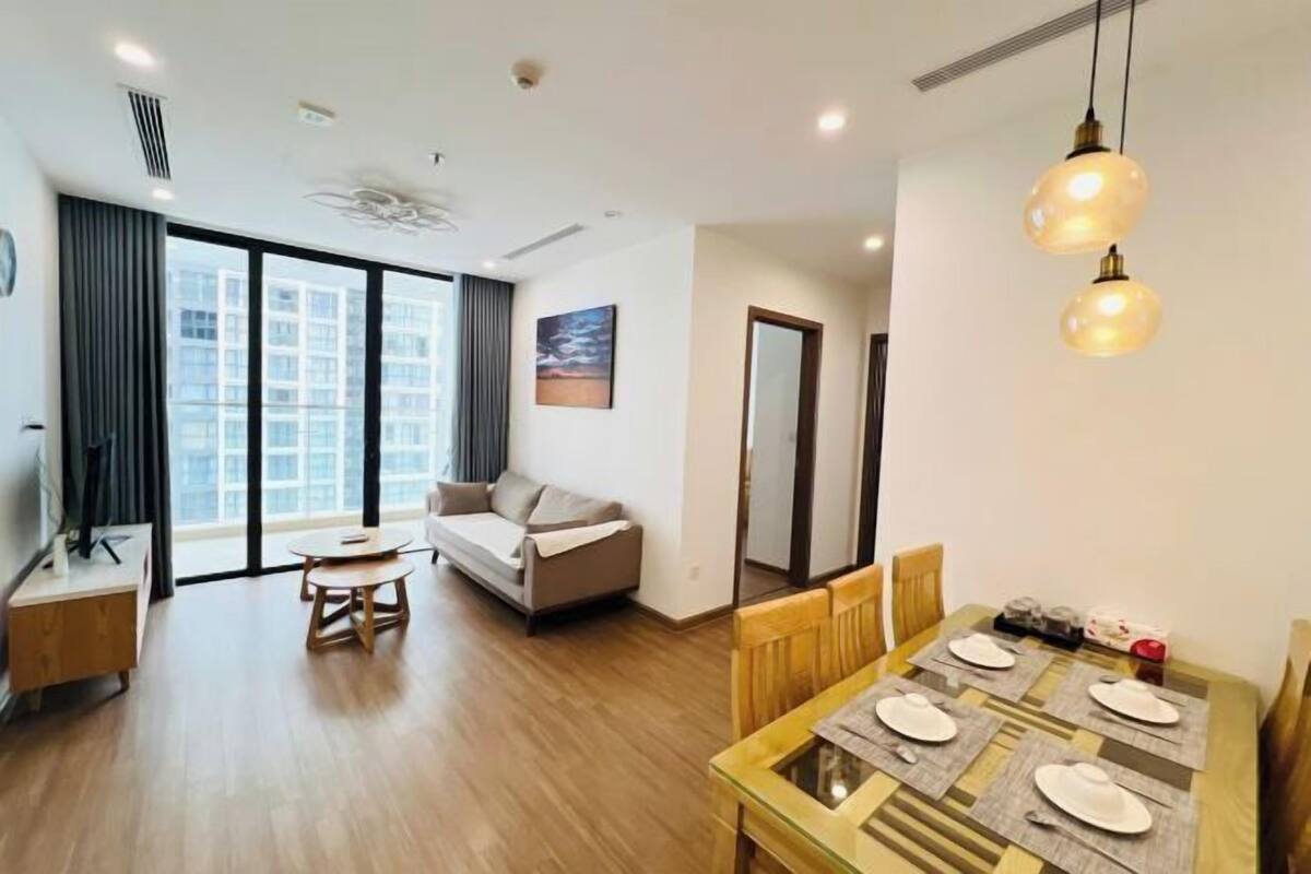 Uma sala de estar moderna com um sofá, uma mesa de jantar posta para quatro pessoas e uma grande janela com vista para edifícios.