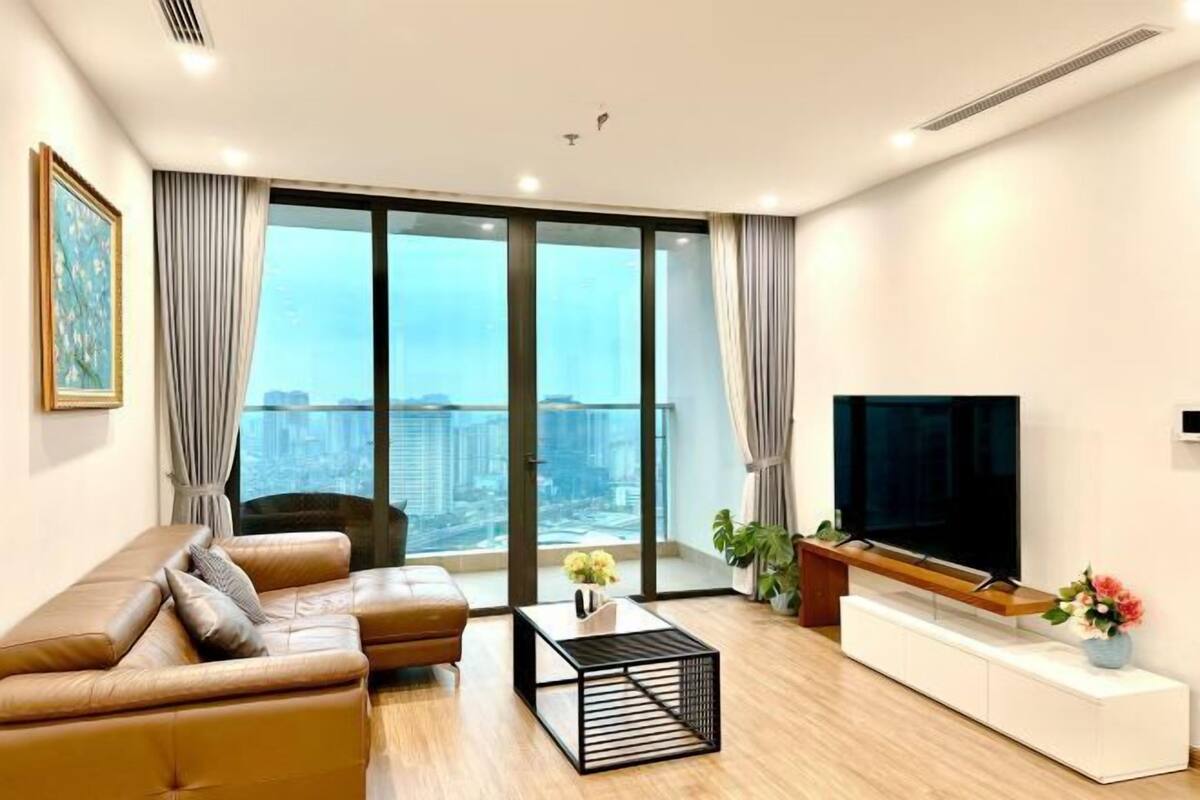 Uma sala de estar moderna com um sofá, uma mesa de centro, uma TV e vista para um horizonte urbano através de grandes janelas.