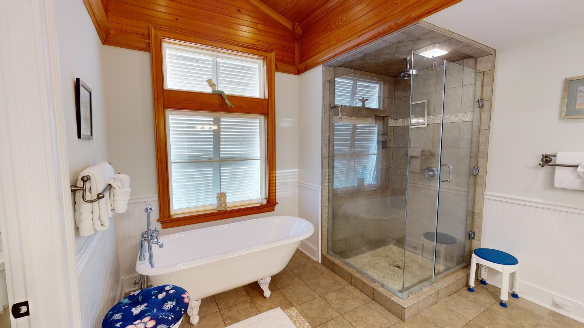 A bathroom with a freestanding bathtub, a glass-enclosed shower, and a small stool.