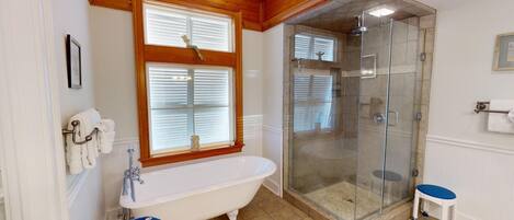 A bathroom with a freestanding bathtub, a glass-enclosed shower, and a small stool.