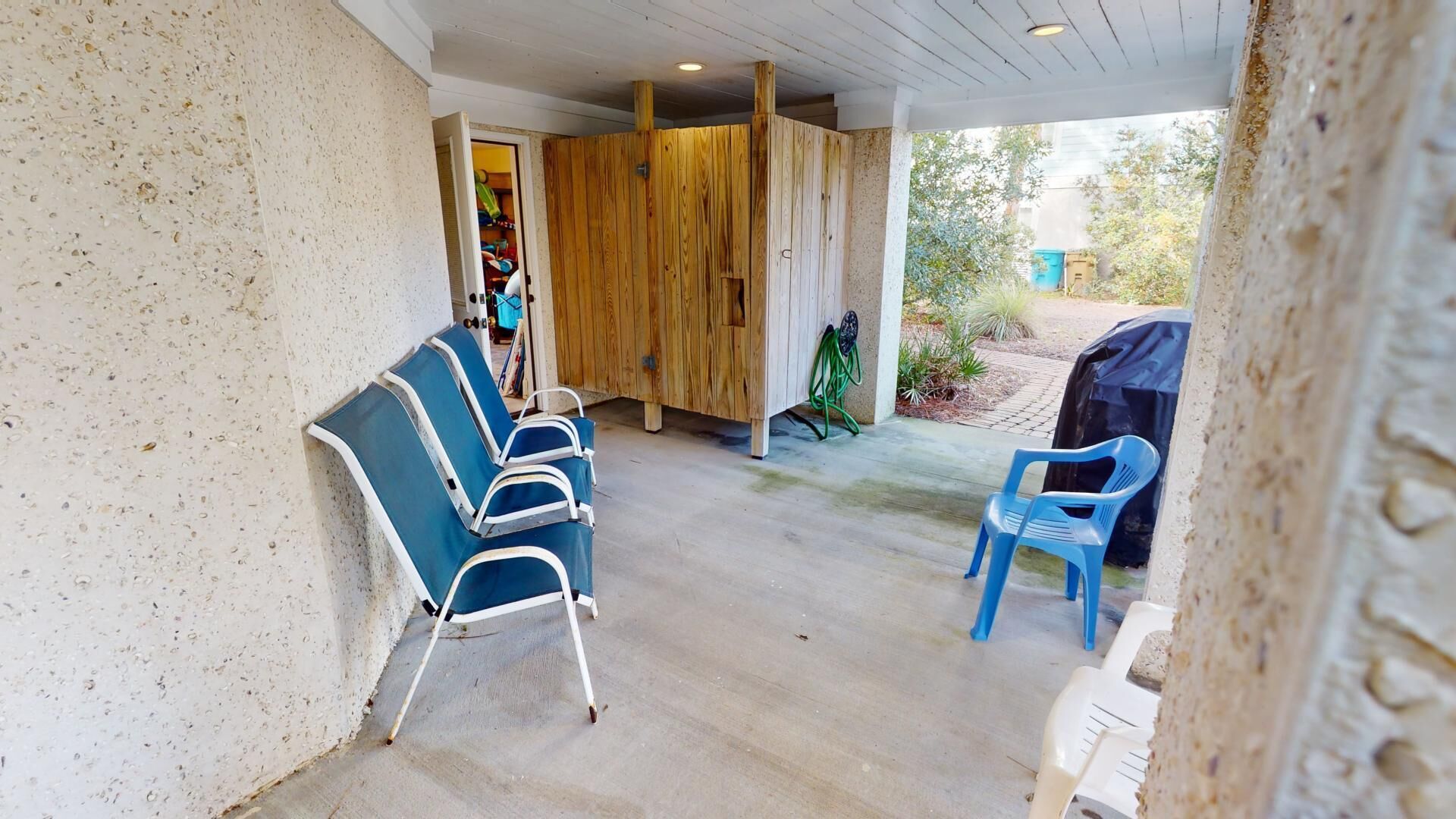 Un espace extérieur abrité, avec des chaises bleues et une cloison en bois.
