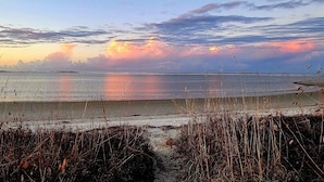 Eine Strandansicht mit hohem Gras im Vordergrund und einem Sonnenuntergang über dem Wasser.