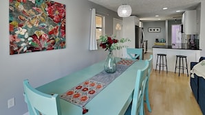 Una cocina moderna con comedor que incluye una mesa y sillas color turquesa, un cuadro floral y una lámpara colgante.