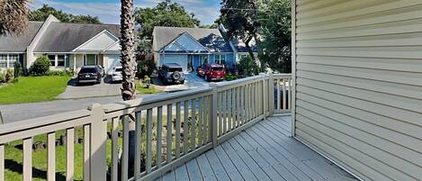 A residential porch with a white railing, a palm tree, and houses in the background.