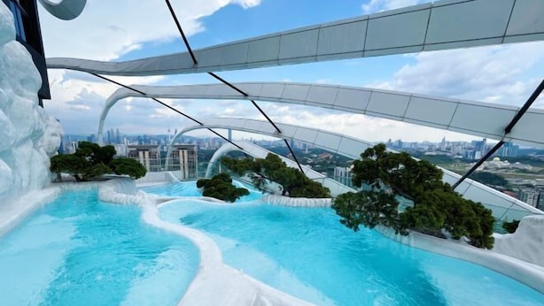 An infinity pool with a cityscape view, surrounded by white structures and greenery. - Arte Mont Kiara By Yan Yee (Kuala Lumpur)