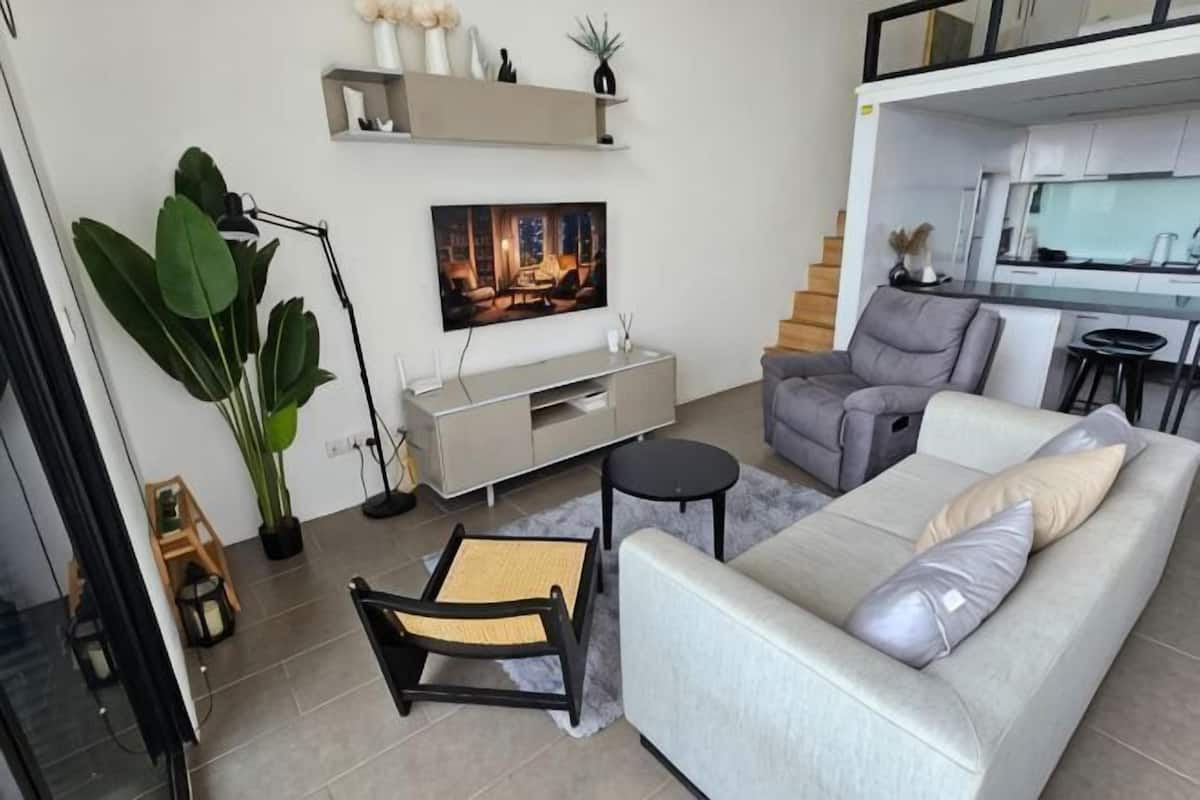 A modern living room with a sofa, TV, and a dining area.