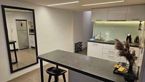 A modern kitchen with a central island, a refrigerator, and a dining area with a chair. - The Establishment Menara Teguh Bangsar Menara UOA KL Sentral (Kuala Lumpur)