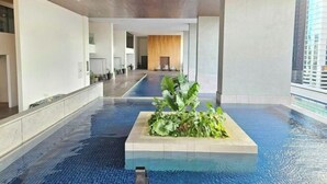 A modern indoor pool area with a central planter, clear blue water, and a view of the building's interior. - The Establishment Menara Teguh Bangsar Menara UOA KL Sentral (Kuala Lumpur)