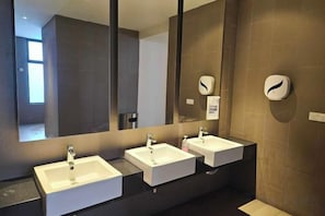 Ein modernes Badezimmer mit drei Waschbecken, einem großen Spiegel und einer Seifenspender.