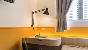 A compact bedroom with a desk, a chair, a bed, a window with curtains, and a wall-mounted TV. - Upstairs Downstairs CoLiving Bukit Bintang (Kuala Lumpur)