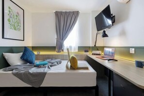 A hotel room with a bed, a desk with a laptop, a TV, and a window with curtains. - Upstairs Downstairs CoLiving Bukit Bintang (Kuala Lumpur)