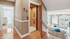 Amplia sala de estar con piso de madera, pared color beige y una escalera que lleva a un balcón con vistas.
