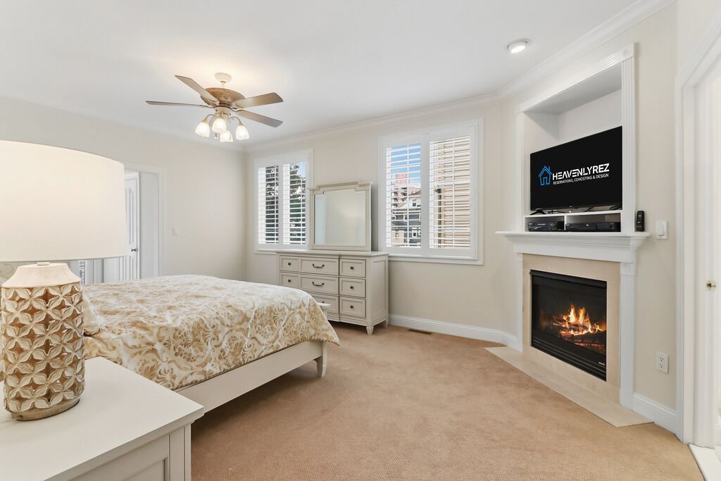 A bedroom with a bed, dresser, TV, fireplace, and windows.