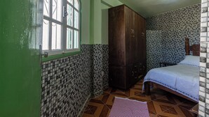 A bedroom with a bed, a wardrobe, a window, and patterned walls and floor.