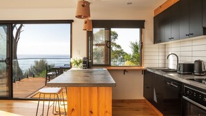 A modern kitchen with a large island, dark cabinets, and a view of the sea. - Rocky Ridge Itas - Hosted by L'Abode (Rocky Hills)