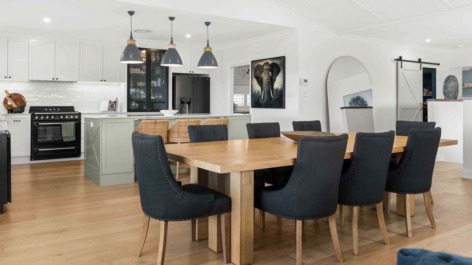 Une cuisine moderne avec des meubles blancs, une cuisinière noire et un coin repas comprenant une table en bois et des chaises foncées.