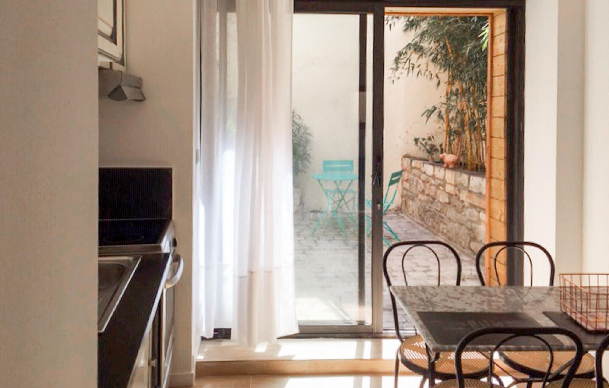 A dining area with a table and chairs, a sliding glass door leading to an outdoor space with a chair and plants.
