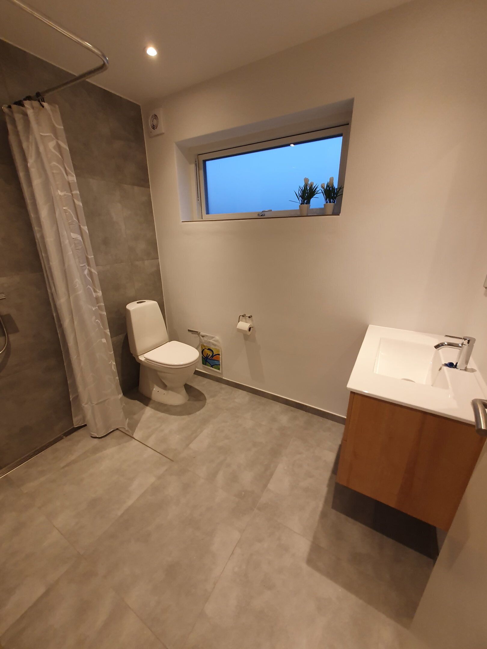 A modern bathroom with a toilet, a window, a sink, and a shower area.