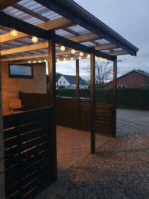 A covered outdoor seating area with a pergola, wooden benches, and string lights.