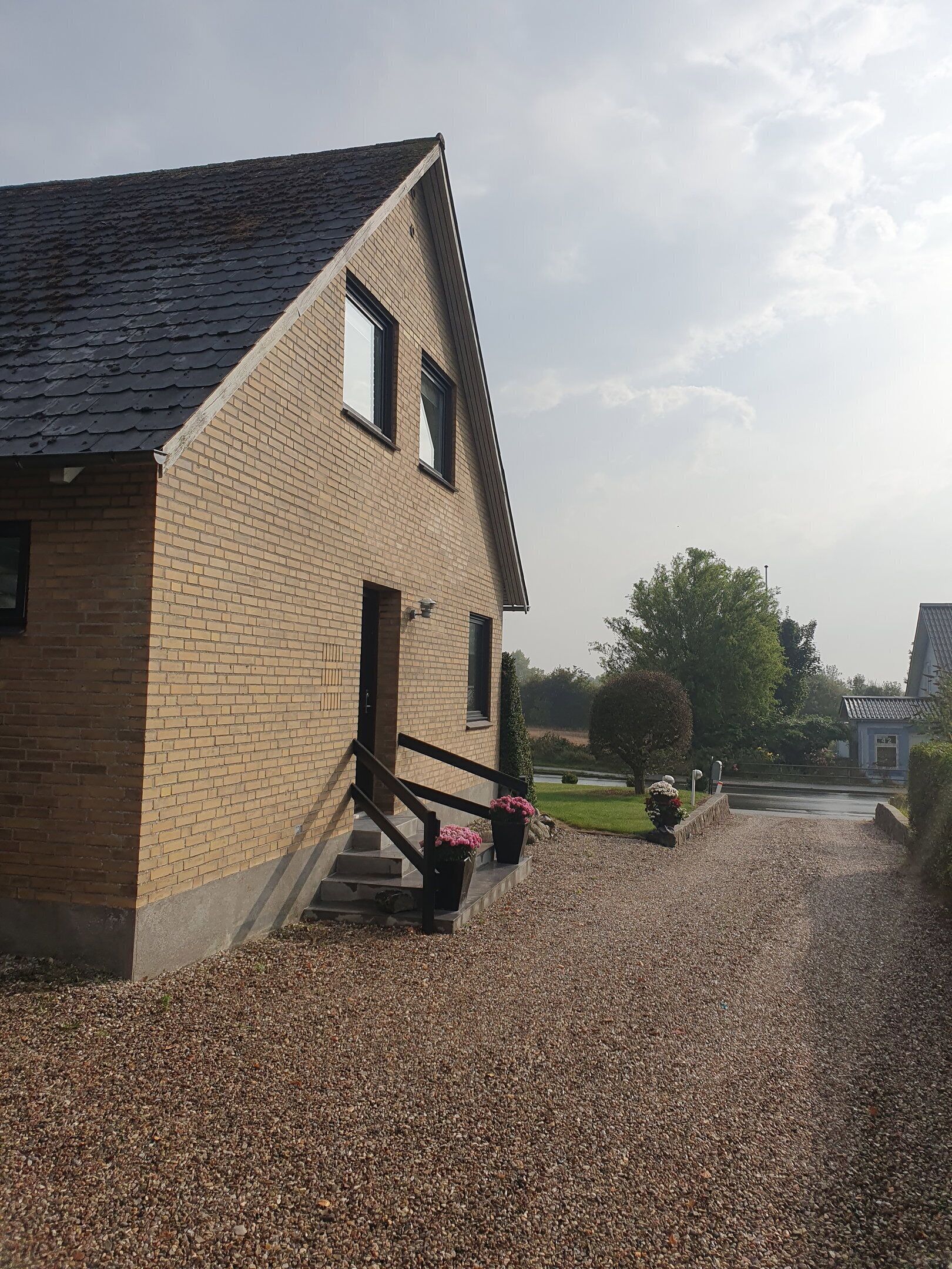 A two-story building with a brick facade, a sloped roof, and a gravel driveway.