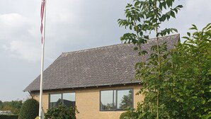 Een huis met een vlaggenmast, een bakstenen gevel en een verzorgd gazon.