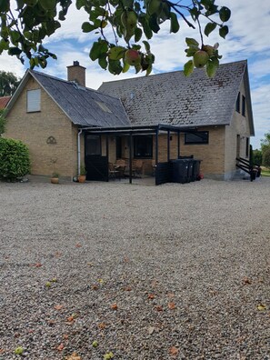 A building with a gravel driveway, a covered outdoor seating area, and a brick chimney. - Lovely holiday home with views of fields (Sydals)