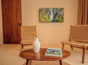 A room with two wicker chairs, a round wooden table, a white vase, and a framed picture on the wall. - High-End 1BR in Veleta · Muunek (Tulum)