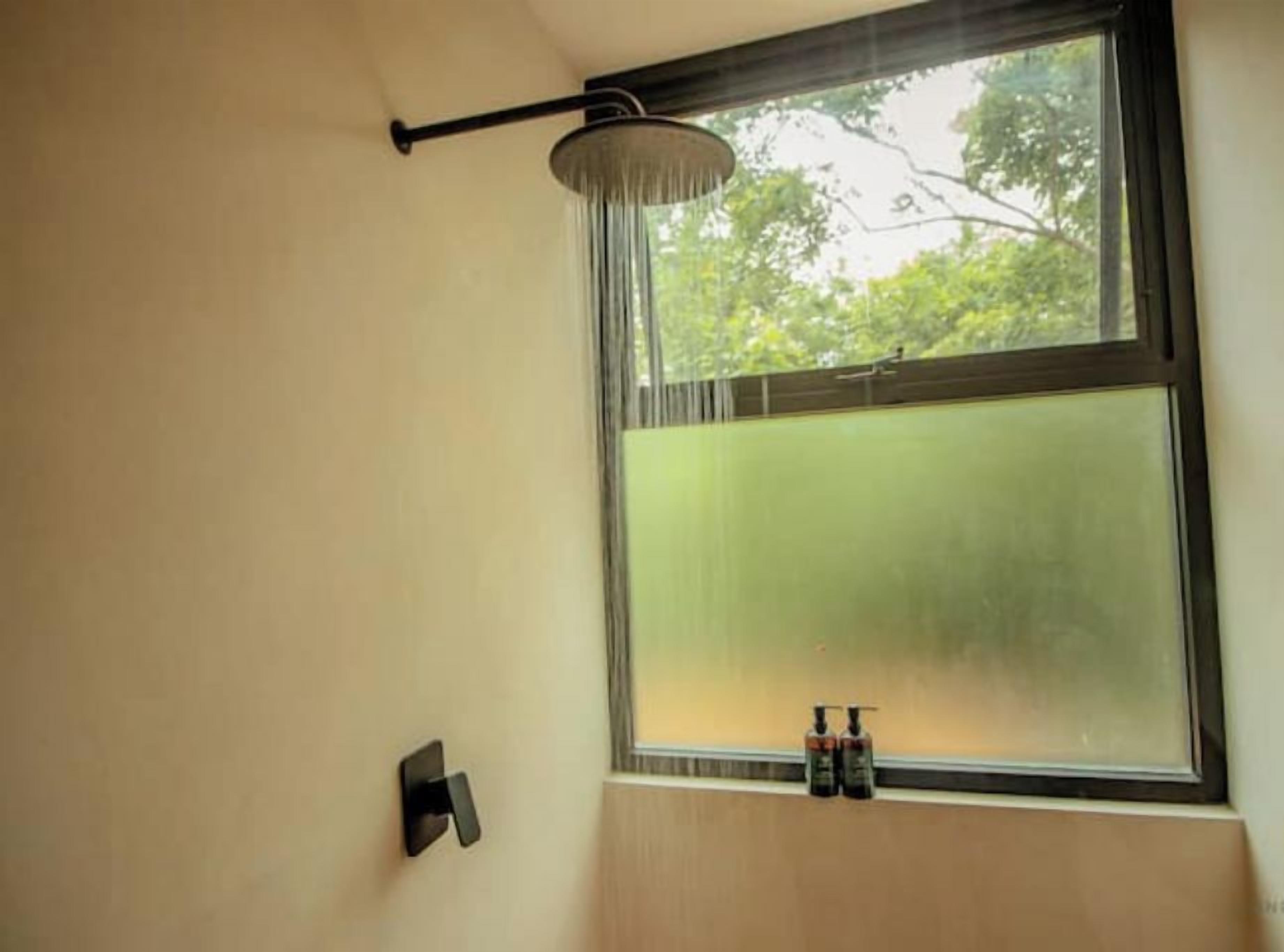 A bathroom with a showerhead above a window, a towel rack, and two bottles on the window sill.
