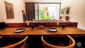Un coin repas avec une table en bois dressée pour deux personnes, un téléviseur et une vue sur la verdure environnante.