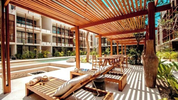 Un espace de détente extérieur moderne, doté de chaises longues en bois, d’une piscine et d’un patio couvert avec un plafond en bois.