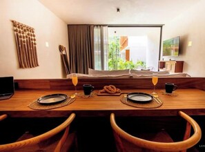 A dining area with a wooden table set for two, a television, and a view of greenery outside. - Deluxe studio in Veleta w/private pool (Tulum)