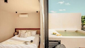 Habitación de hotel con cama, una mesita con un libro y vistas a una piscina y vegetación.